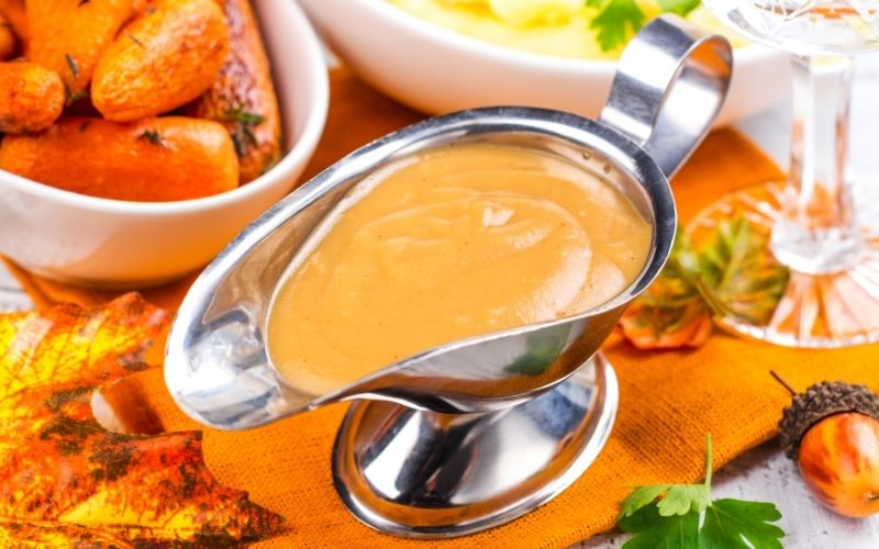 Gravy sauce on Thanksgiving day decorated table. Mashed potatoes and roasted baby carrots - traditional side dishes | Easy Turkey Gravy Recipe | Thanksgiving recipe
