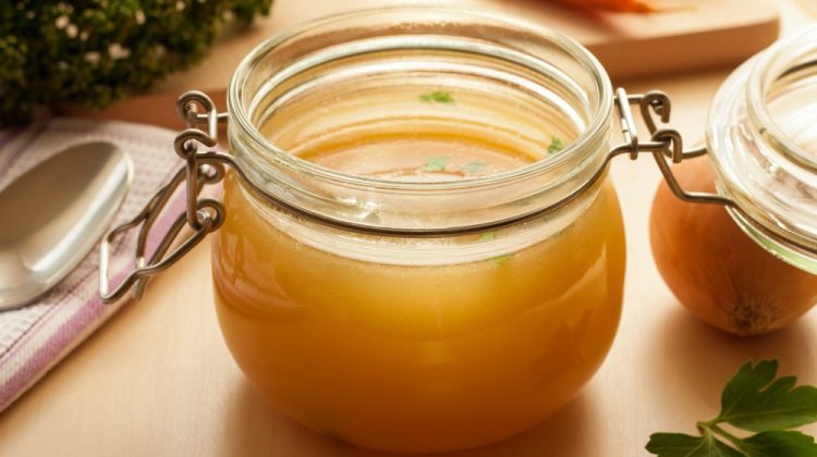 Bone broth made from chicken in a glass jar, with carrots, onions, and parsley in the background | Make This Easy Homemade Bone Broth Recipe (+ Benefits) | bone broth recipe | Featured