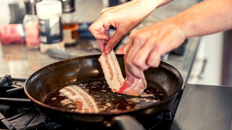 person holding a strip of bacon ready to fry | How To Fry Food Without Oil Splatter | Featured