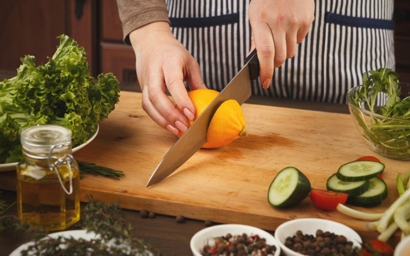 woman with knife cutting lemon on wooden board | kitchen knife
