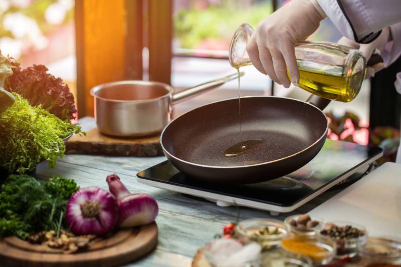 person pouring an olive oil on pan | How To Fry Food Without Oil Splatter | splatter guard
