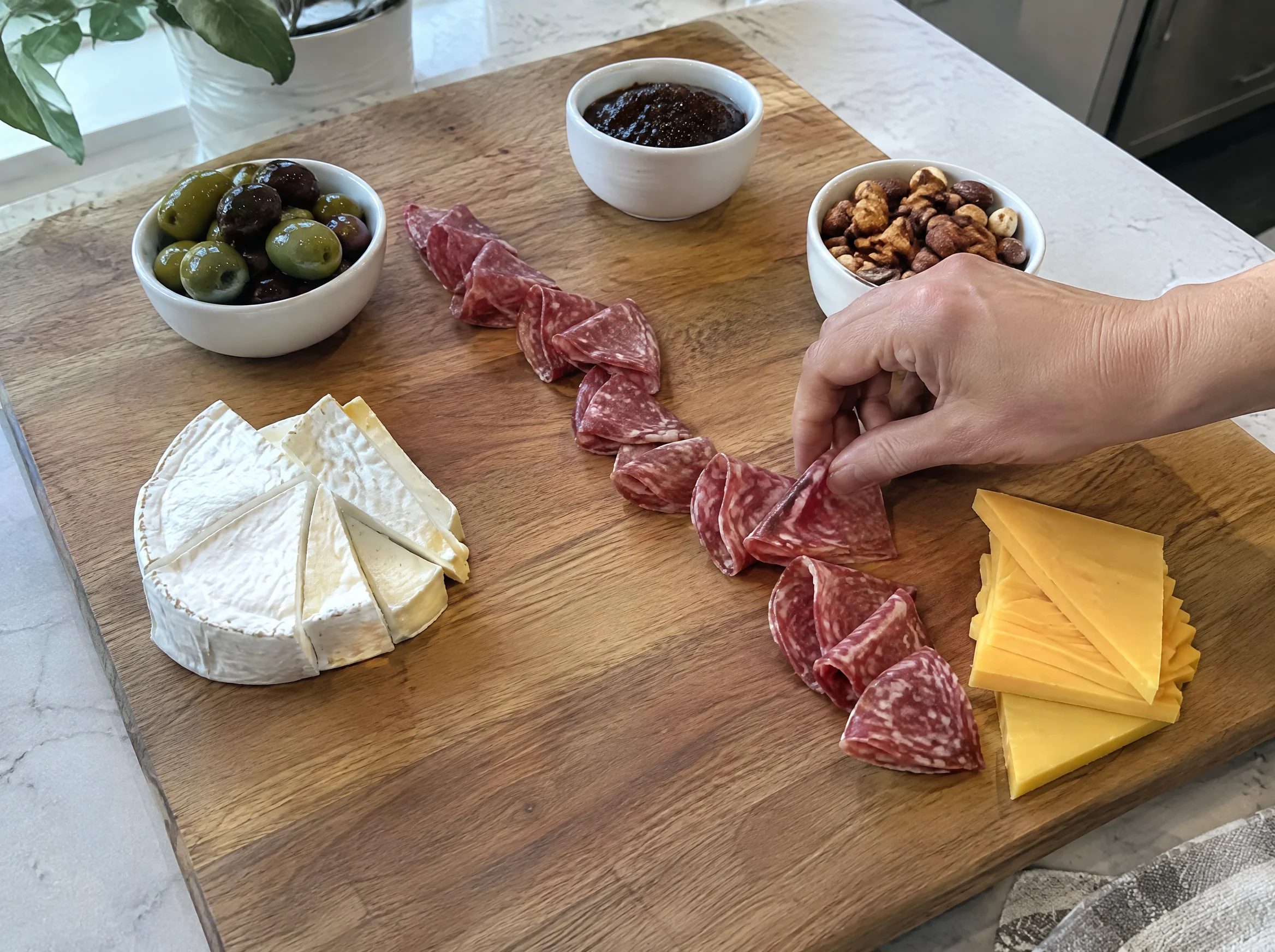 Laying folded salami between cheeses on a half-built Christmas charcuterie board